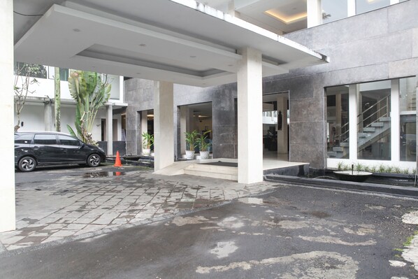 A modern building entrance with a paved driveway, a parked car, and potted plants. - Reddoorz Premium @ Ciumbuleuit Atas (Bandung)