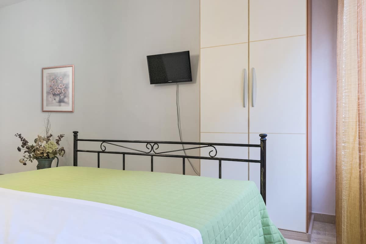 Een slaapkamer met een bed, een aan de muur bevestigde televisie, een kledingkast en een ingelijst kunstwerk.