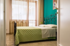 Quarto com cama, janela com cortinas leves e parede azul-turquesa.