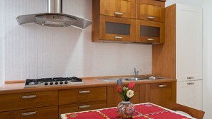Een keuken met houten kastjes, een gasfornuis, een spoelbak en een tafel met een rode tafelkleed.