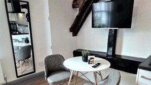 A modern living room with a white round table, two grey armchairs, a black TV mounted on the wall, and a wooden staircase.