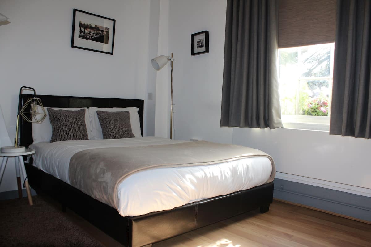 A bedroom with a bed, a nightstand, a floor lamp, and a window with curtains.