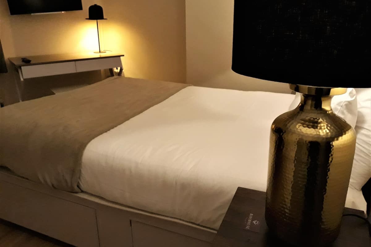 A hotel room with a bed, a bedside table, a lamp, and a television mounted on the wall.