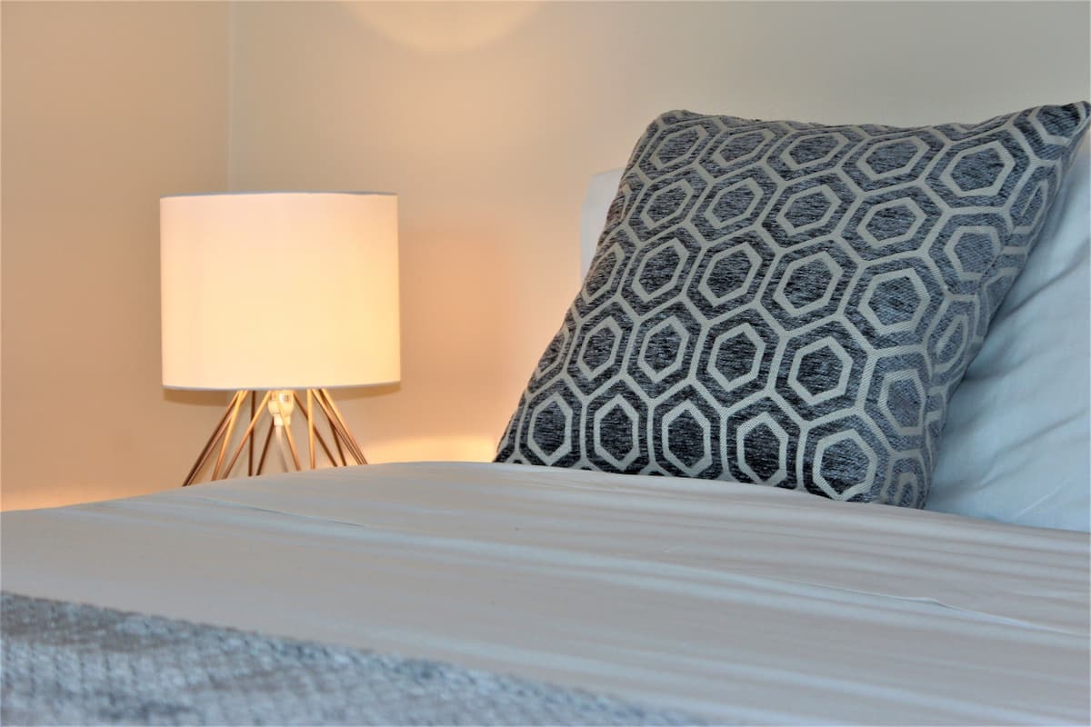 A neatly made bed with a patterned pillow and a bedside lamp.