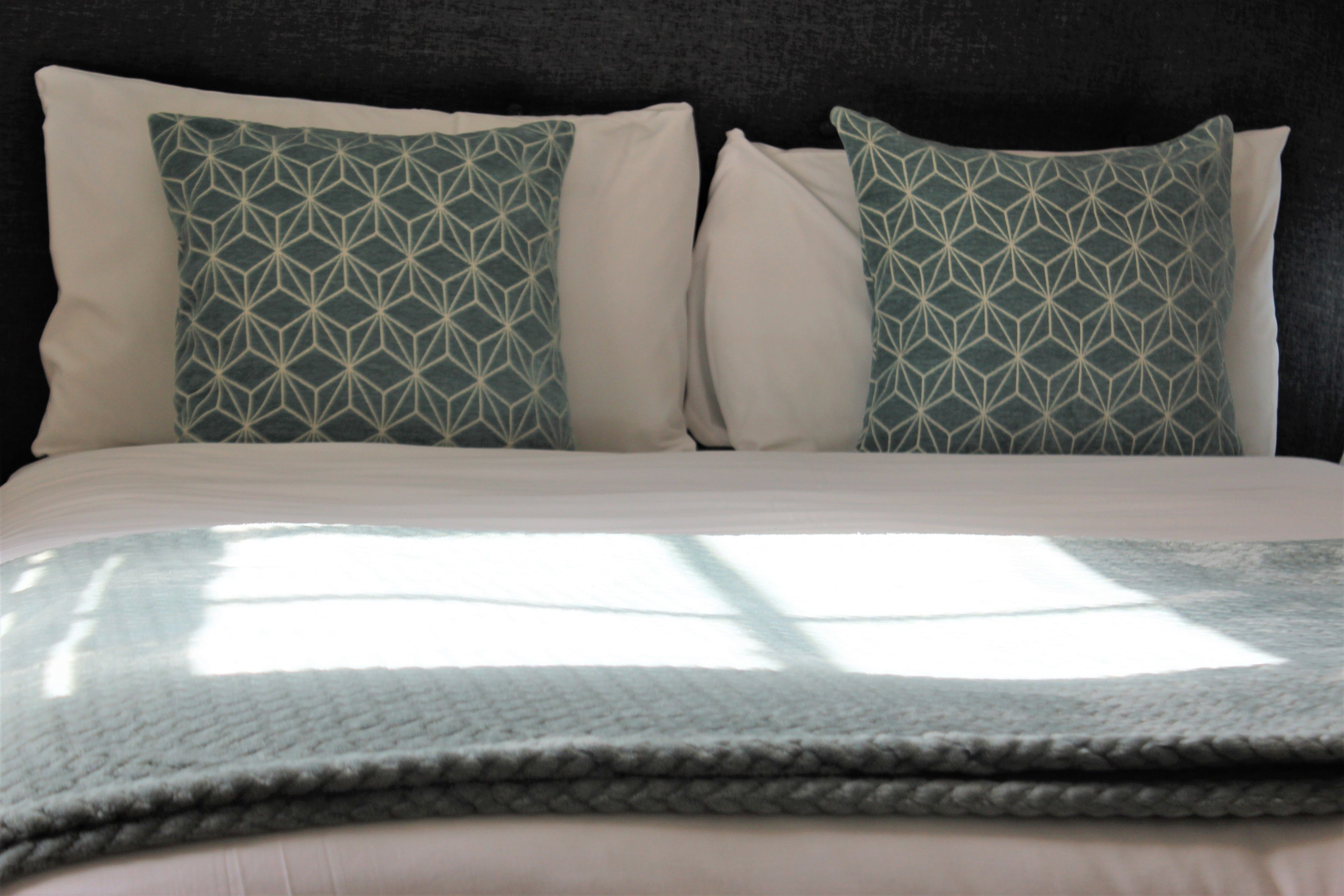 Cama com conjunto de almofadas brancas e azul-turquesa em frente a uma parede escura.