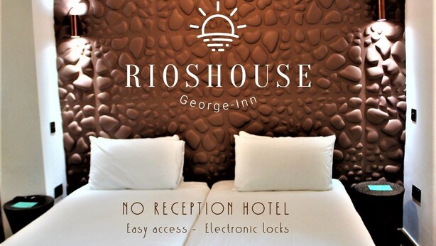 A hotel room with a textured wall, two white beds, and a logo for Rioshouse George-Inn. It mentions no reception and easy access with electronic locks.