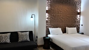 A modern hotel room with a bed, a sofa, a lamp, and a textured wall.