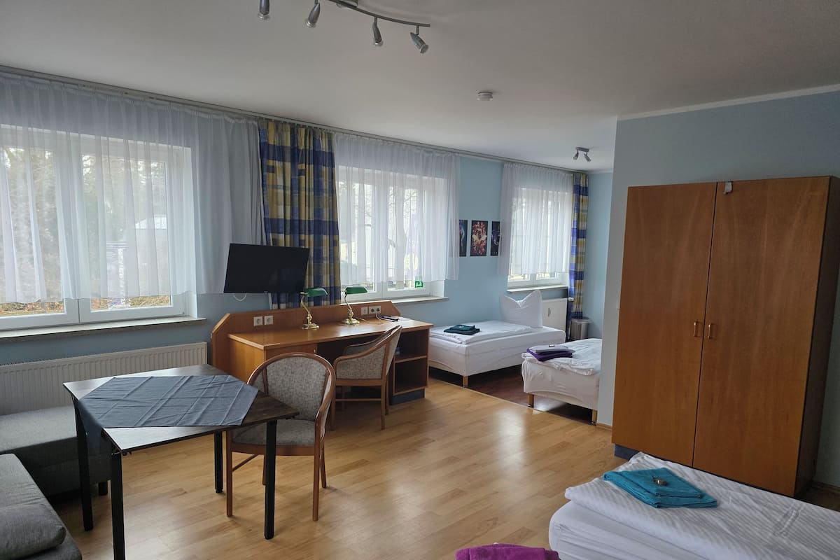 A hotel room with a bed, a desk with a computer, a chair, a wardrobe, and a window with curtains.