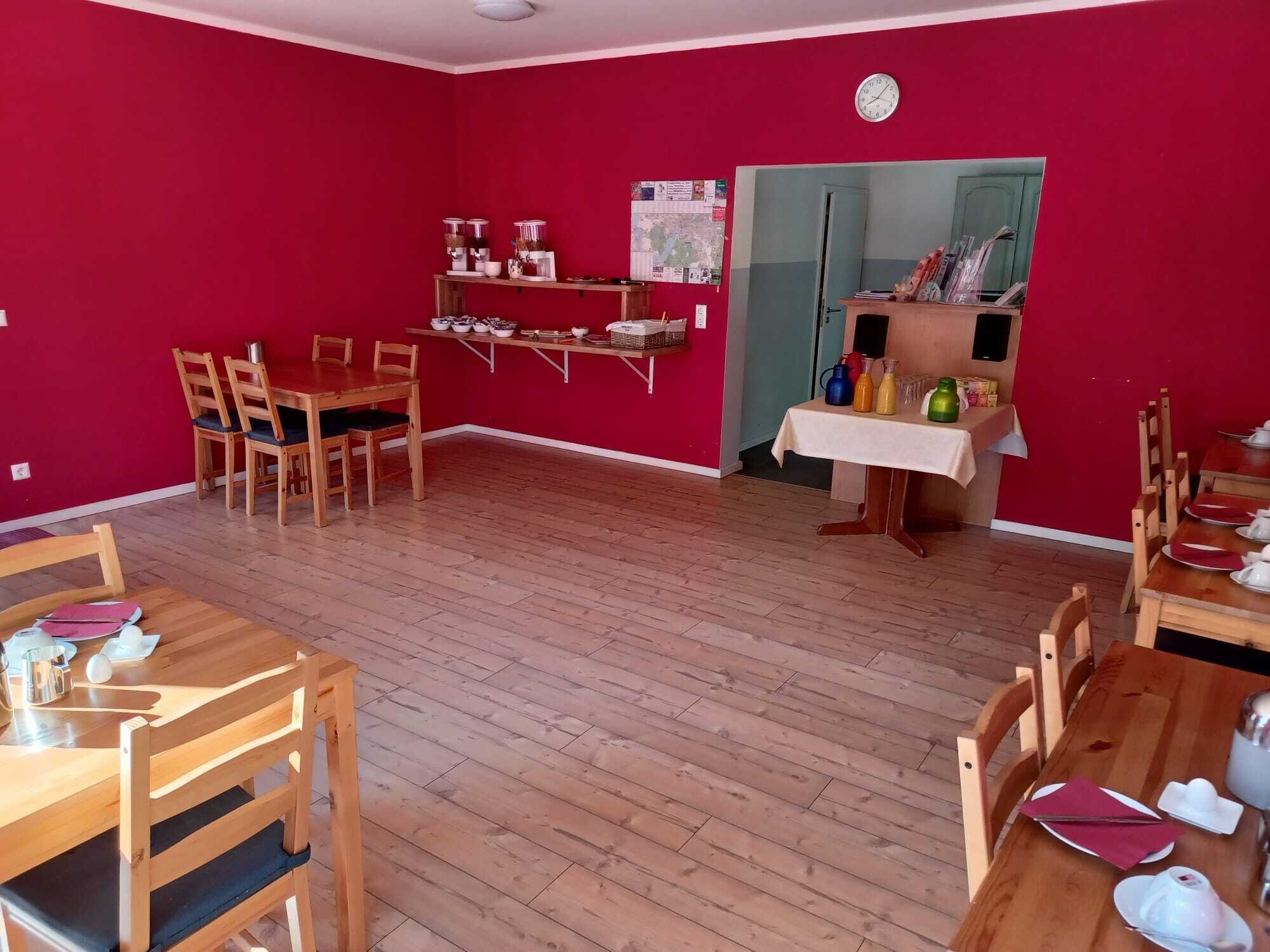 A dining area with wooden tables and chairs, a shelf with kitchenware, and a clock on the wall.