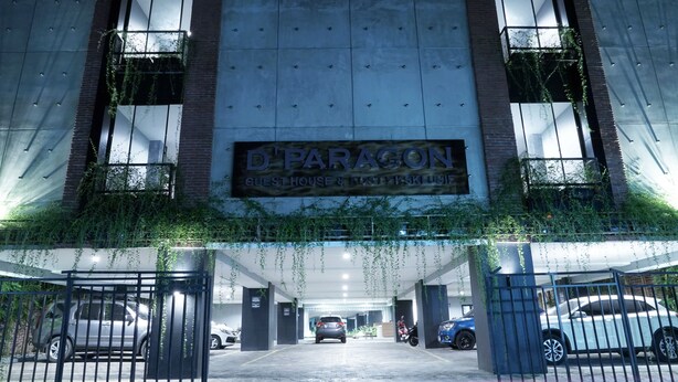 Un edificio con un letrero que dice "D'PARAGON GUEST HOUSE & RESTAURANT" y una entrada protegida por una reja, con coches aparcados.
