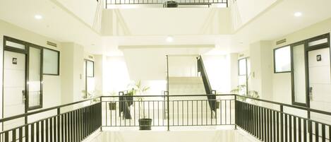 A multi-level atrium with glass ceilings, black railings, and potted plants.