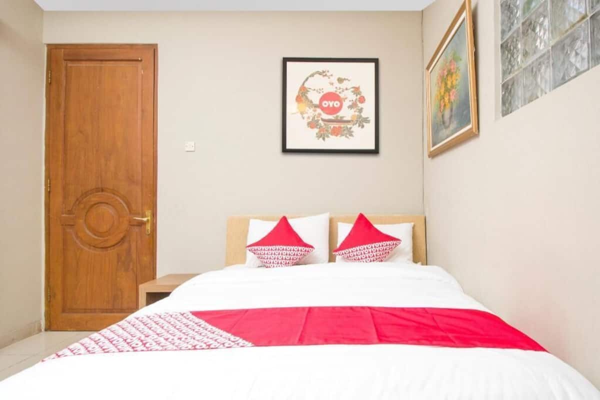 A bedroom with a wooden door, a bed with white and red bedding, and a framed picture on the wall.
