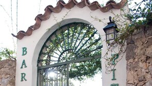 A restaurant entrance with a green gate, potted plants, and outdoor seating visible through the gate. - Mimì B&B (Ravello)