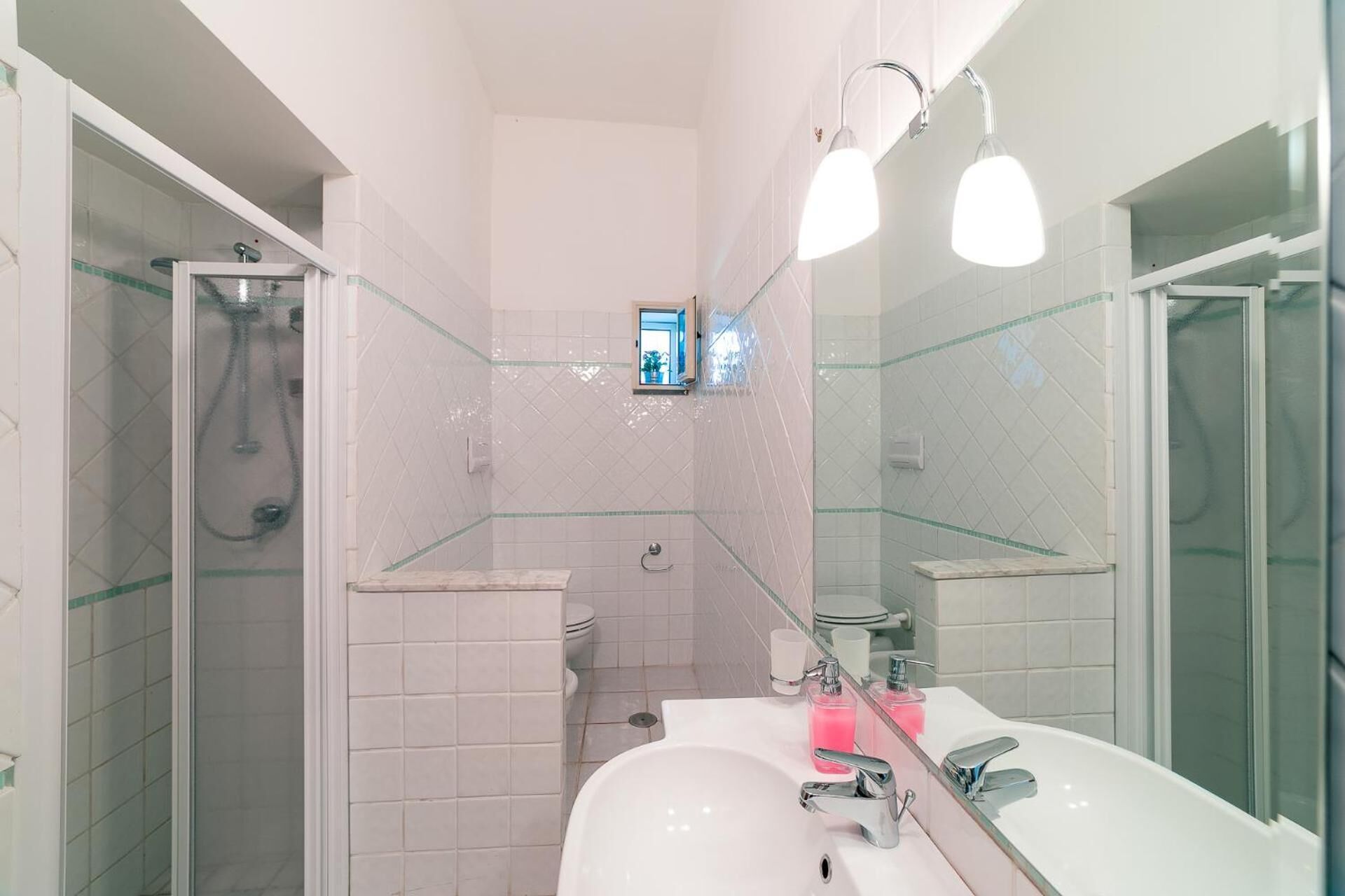 Ein Badezimmer mit einer Duschkabine, einem weißen Waschbecken mit Spiegel und einer Toilette.