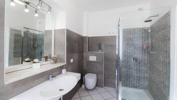 Un baño moderno con un espejo grande, un lavabo blanco, un inodoro y una zona de ducha con mampara de vidrio.