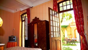 A room with a bed, a television, a wardrobe, and a door leading to an outdoor patio with tables and chairs. - Hotel Du Fiacre (Carpentras)