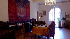 A dining area with a round table, chairs, a chandelier, and a large tapestry on the wall. - Hotel Du Fiacre (Carpentras)