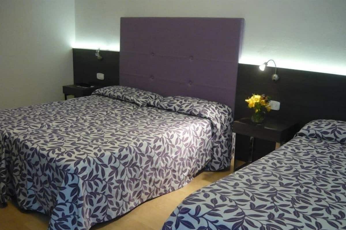 A hotel room with two beds, each with a patterned bedspread, a headboard, bedside tables, and a nightstand with a vase of flowers.
