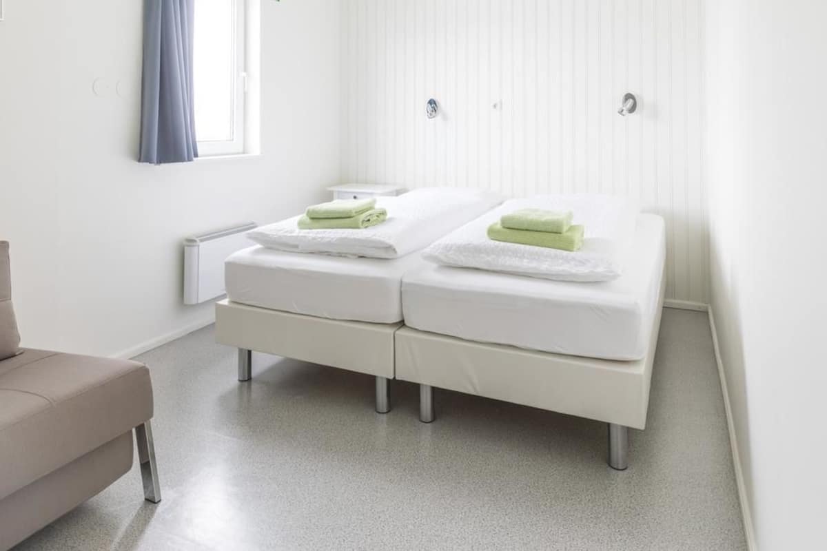Een moderne, schone kamer met twee bedden, een klein nachtkastje en een bankje.