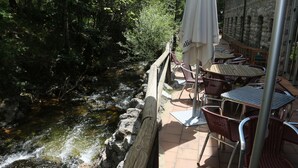 A riverside patio with outdoor seating and a stone wall backdrop. - Balneario  Caldas de Luna (Sena de Luna)