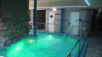 Una piscina cubierta, una piscina con cascada, tumbonas