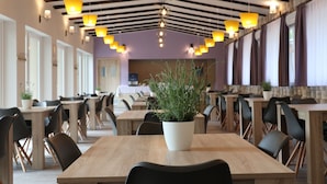 A modern dining area with wooden tables and black chairs, featuring pendant lighting and a central potted plant. - The Hotel Unforgettable - Hotel Tiliana by Homoky Hotels & Spa (Budapest)