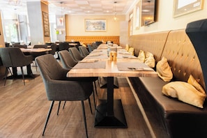 A restaurant with a long wooden table, cushioned benches, and modern chairs.