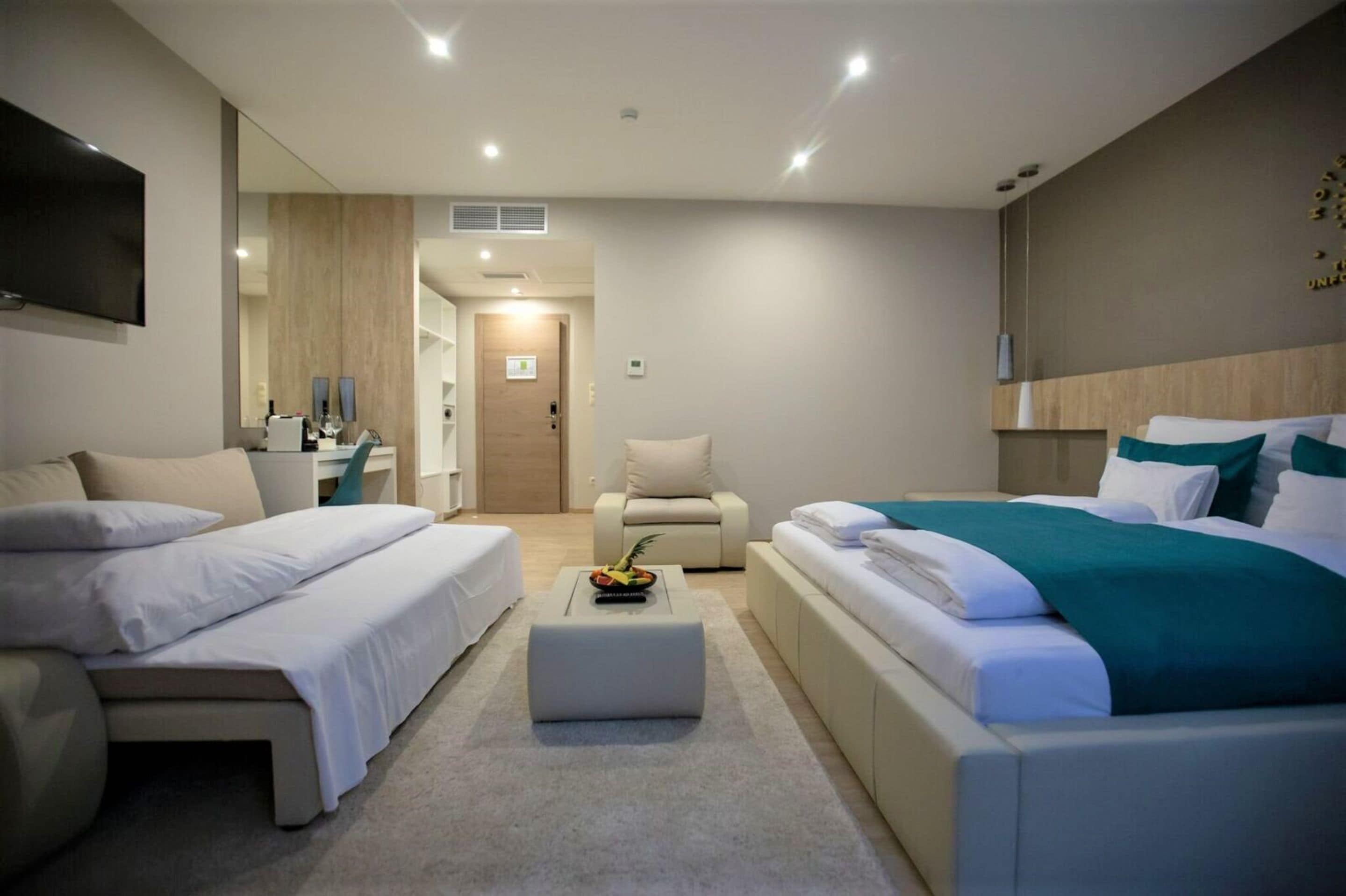 A modern hotel room with two beds, a seating area, a TV, and a bathroom visible through an open door.
