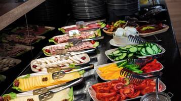 Ein reichhaltiges Buffet mit verschiedenen Speisen, darunter Fleisch, Käse, Obst und Soßen.