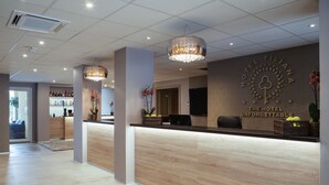 A hotel reception area with a modern design, featuring a wooden reception desk, a chandelier, and a wall-mounted sign. - The Hotel Unforgettable - Hotel Tiliana by Homoky Hotels & Spa (Budapest)