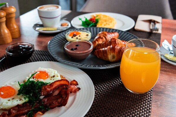 Desayuno con platos de huevos, tocino, croissants y zumo de naranja.