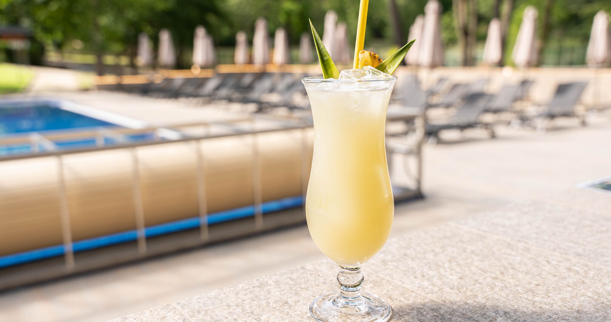 A cocktail glass with a straw and a garnish on a poolside setting.