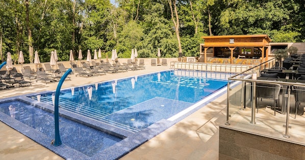 A swimming pool with lounge chairs and umbrellas, surrounded by trees.