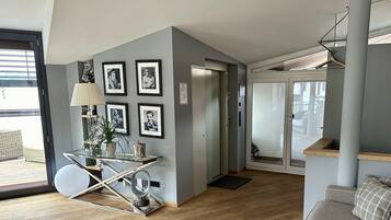 Ein modernes Wohnzimmer mit einem Glastisch, gerahmten Bildern an der Wand, einem Sofa und einer Treppe, die zu einer oberen Etage führt.