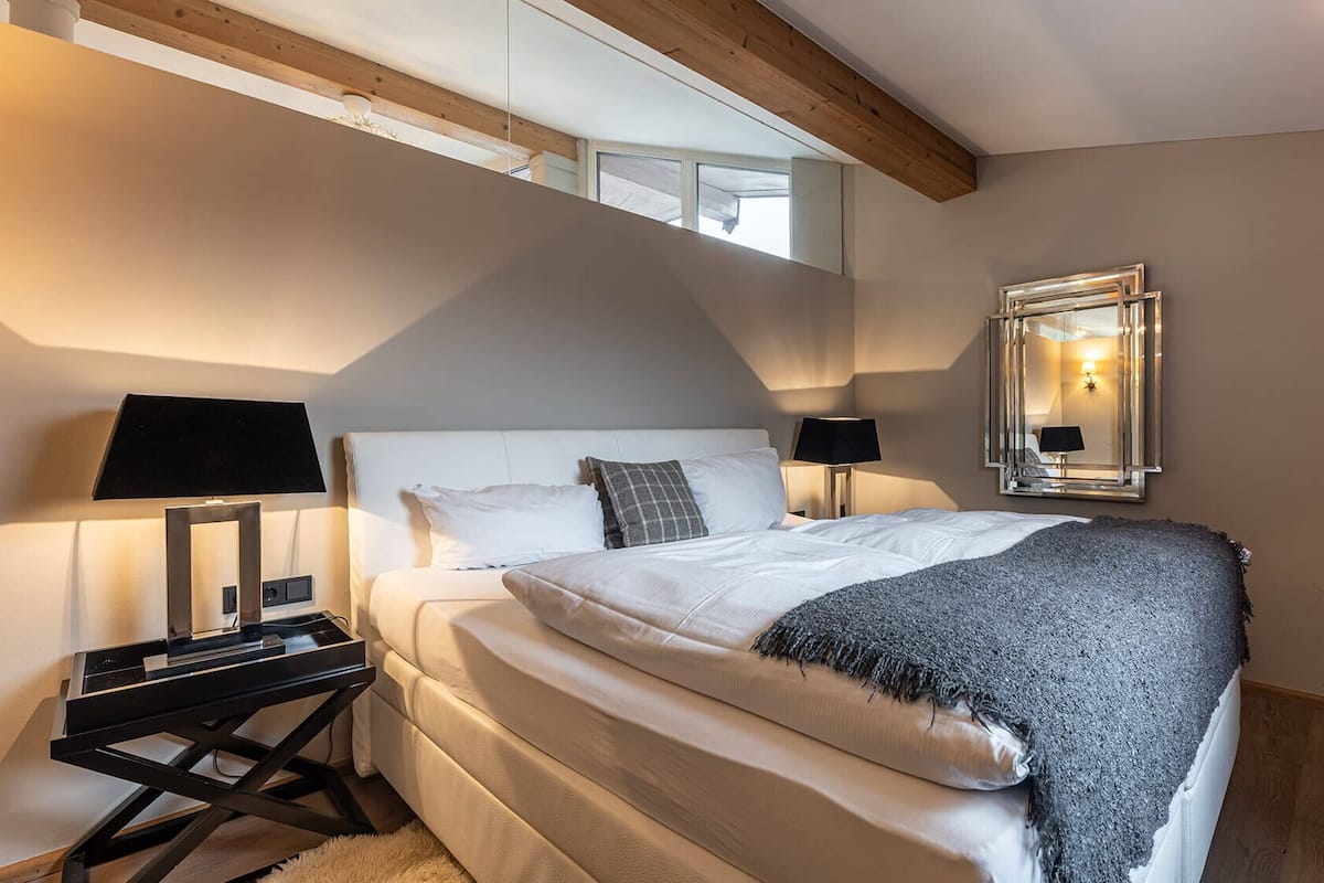 A bedroom with a bed, two bedside tables, a mirror, and a window.