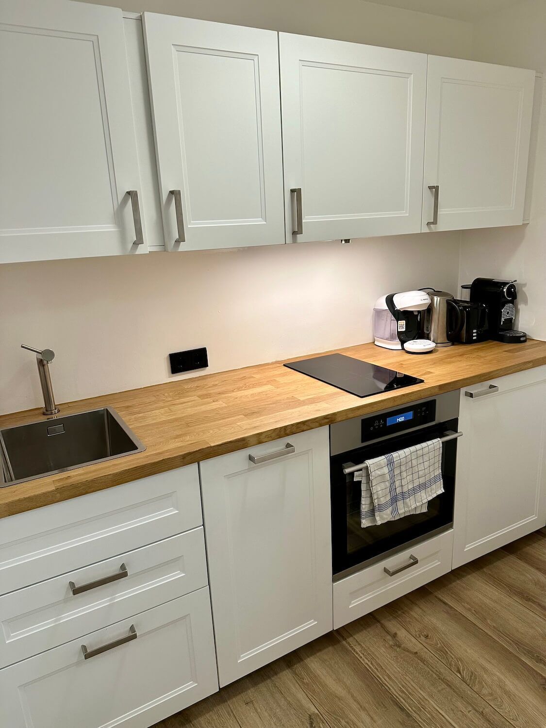 Una cucina moderna con pensili bianchi, un piano di lavoro in legno, un lavello in acciaio inossidabile, una macchina da caffè e un forno.