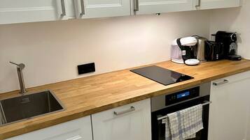 A modern kitchen with white cabinets, a wooden countertop, a stainless steel sink, a coffee maker, and an oven.