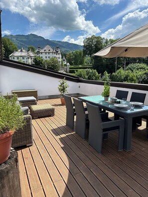 A wooden deck with wicker furniture and a table set for dining, overlooking a mountainous landscape.