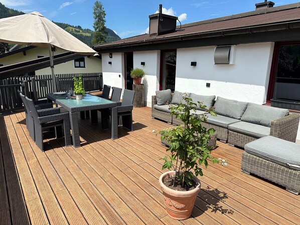 A wooden deck with outdoor furniture, including a table and chairs, and a sofa.