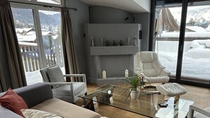 Una sala de estar moderna con un sofá, sillones, una mesa de centro de vidrio y una chimenea con adornos decorativos.