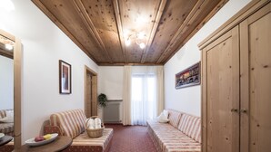A cozy room with a wooden ceiling, a sofa, a small table with a plate of fruit, and a radiator. - Alpenhof (Ultimo)