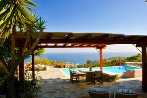 Un espace aménagé au bord de la piscine, doté d’une pergola, de sièges d’extérieur et offrant une vue sur la mer.