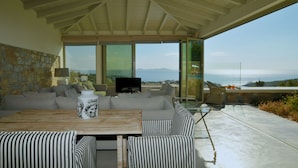 A modern living room with a large TV, comfortable seating, and a view of the ocean. - Paparouna (Alonissos)