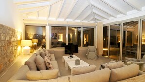 A spacious living area with a high ceiling, a stone wall, a sofa set, a coffee table, and a television. - Paparouna (Alonissos)