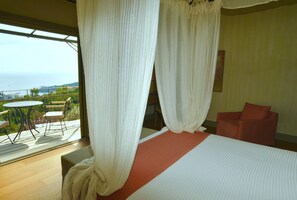 Un dormitorio con una cama grande, un balcón con sillas y vistas al mar.