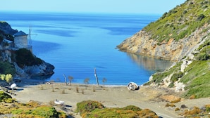 A coastal landscape with a rocky shoreline, a small building with a tower, and a clear view of the sea. - Paparouna (Alonissos)