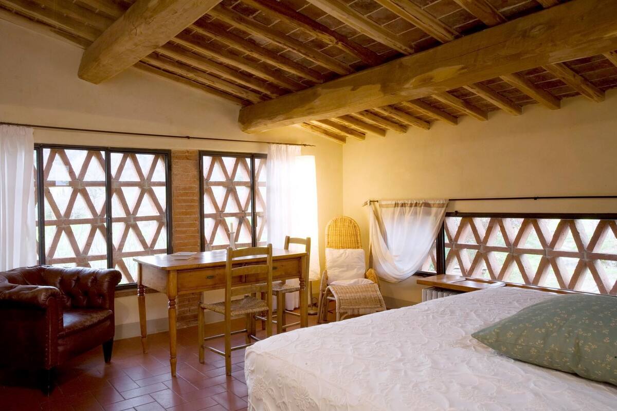 Ein Schlafzimmer mit Holzboden, einem Bett mit grünem Kissen, einem Holztisch mit Stuhl und einem Ledersofa.