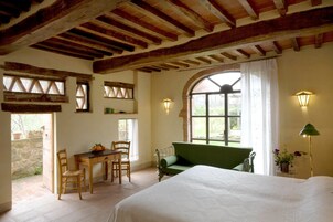 Un dormitorio con cama, un sofá verde, una mesa de madera con sillas y una ventana con cortinas.