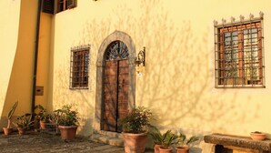Un bâtiment doté d’une grande porte en bois, de plantes en pot et d’un banc en pierre.