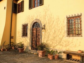 A building with a large wooden door, potted plants, and a stone bench.